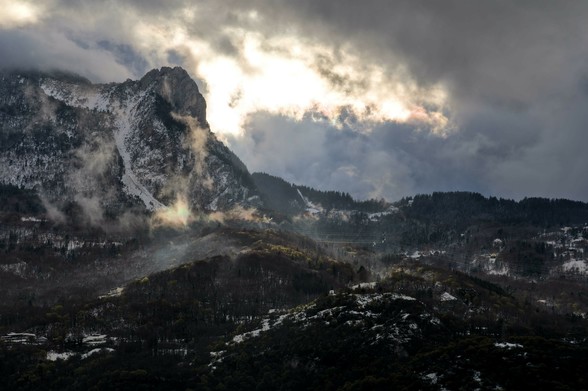 Vue hivernale sur le vercors avec de la neige dispersée à basse altitude et dense à haute altitude, des nuages fins sur les collines qui reflètent la lumière du soleil, et une trouée dans les nuages derrière l’éperon rocheux des trois pucelles.